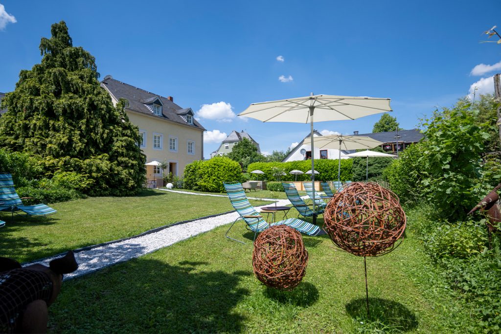 Außenbereich des Wein- & Tafelhaus. Zu sehen sind liegen und Sonnenschirme